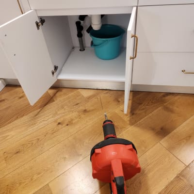 כלי עבודה אדום על רצפה ליד ארון פתוח עם דלי