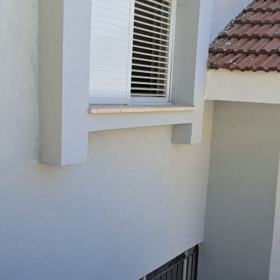 חלון עם תריסים לבנים על קיר צבוע אפור