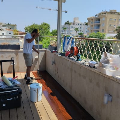 אדם צובע דק עץ במרפסת עם רולר וצבע