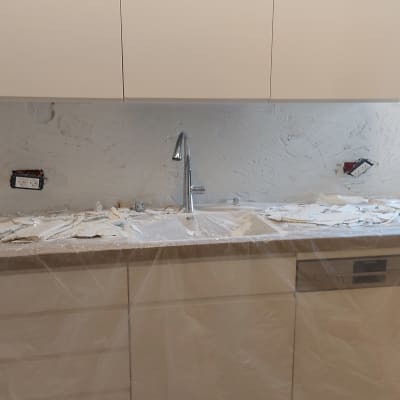 מטבח בשיפוץ עם כיור, קיר חשוף וארונות מכוסים בניילון