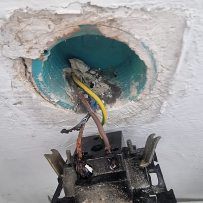 חוטי חשמל חשופים בקיר עם שקע מפורק