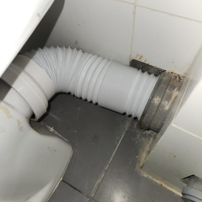 צינור לבן מחובר לאסלה על רצפת אריחים אפורה