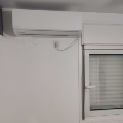 Air conditioner mounted on a white wall above a window.