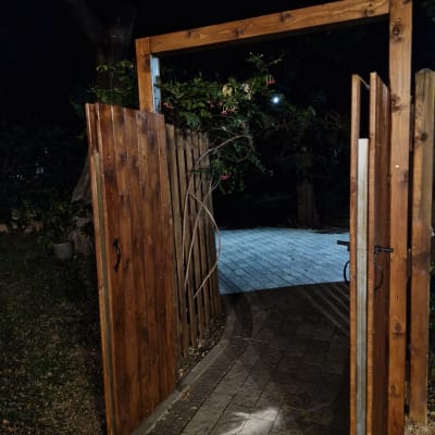 שער עץ פתוח עם צמחייה מסביב בלילה