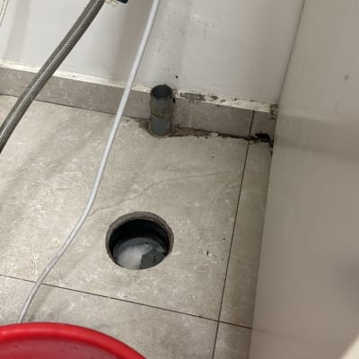 דלי אדום עם מים וסבון ליד צינור ביוב פתוח