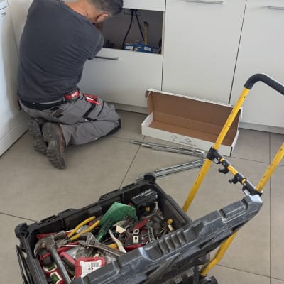 אדם עובד מתחת לכיור במטבח עם כלי עבודה