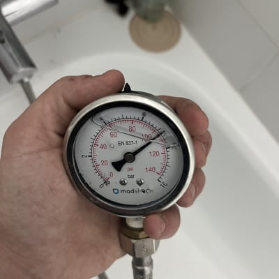 מד לחץ מים מוחזק ביד מעל אמבטיה