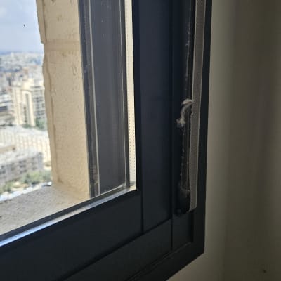 חלון עם תריסים חלקיים ונוף עירוני ברקע