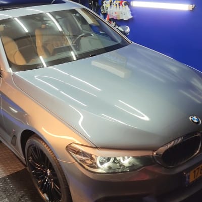 רכב אפור מבריק עם פנסים דולקים בחדר דיטיילינג