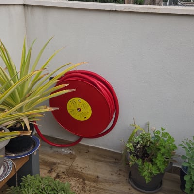 גלגלת כיבוי אש על קיר עם צמחים מסביב