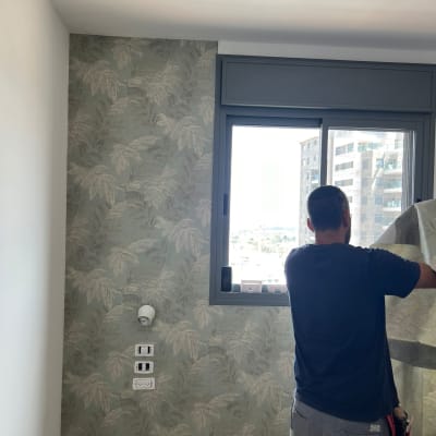 אדם מתקין טפט עם דוגמת עלים על קיר