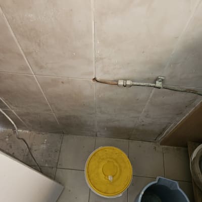 צינור דולף בקיר עם דלי ומגב על הרצפה