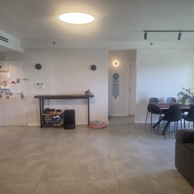 חדר מגורים עם שולחן אוכל וכיסאות, קיר לבן ותאורה