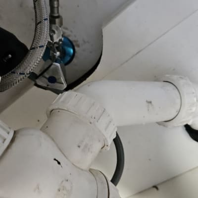 צינור פלסטיק לבן עם חיבורים מתכתיים מתחת לכיור
