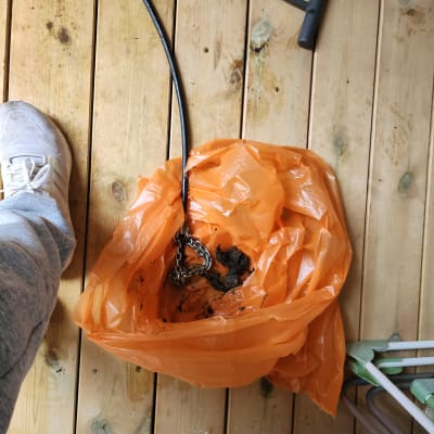 שקית כתומה עם שרשרת וכלי עבודה על רצפת עץ