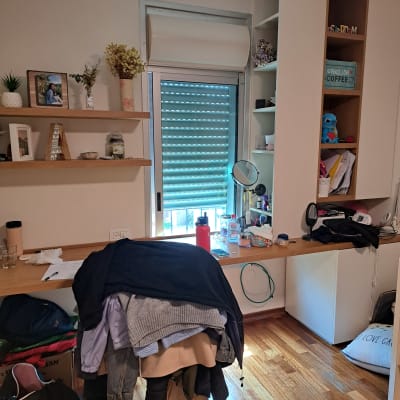 חדר עם מדפים, שולחן עמוס, בגדים על כיסא, ארון פתוח