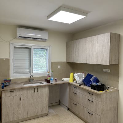 מטבח עם ארונות עץ, כלים וחומרי ניקוי על השיש