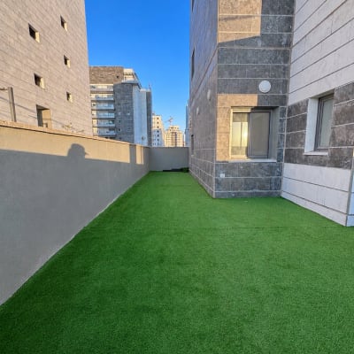 מרפסת עם דשא סינתטי בין בניינים גבוהים