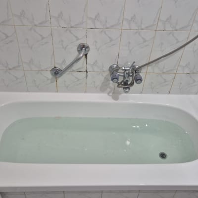 אמבטיה עם מים, ברז ומוט אחיזה על קיר מרוצף