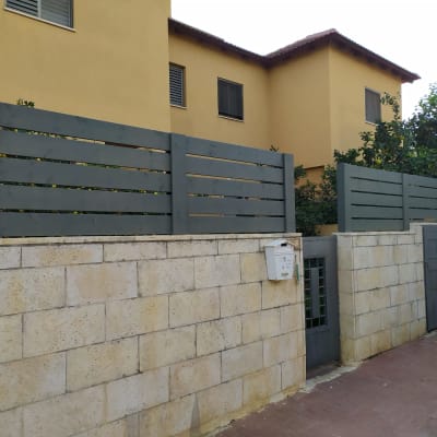 גדר עץ אפורה על קיר אבן בגינה