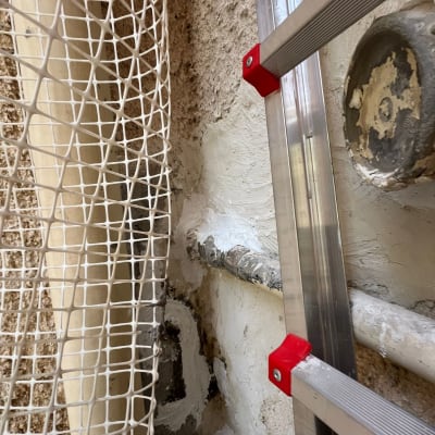 צינור אטום עם חומר איטום לבן ליד סולם מתכת