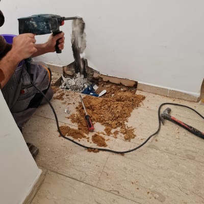 אדם משתמש במקדחה בקיר עם כלים על הרצפה