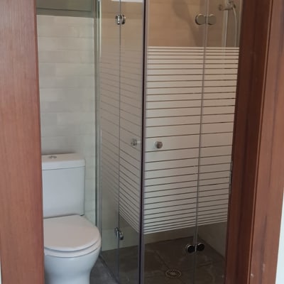 מקלחון זכוכית עם ראש מקלחת, שירותים ורצפת קרמיקה