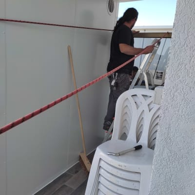 אדם על סולם ליד קיר עם מטאטא וכיסאות פלסטיק