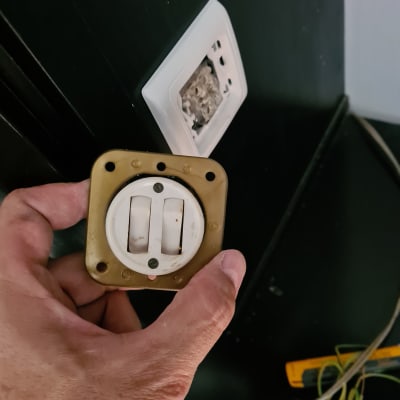 יד מחזיקה מתג חשמלי ישן ליד שקע פתוח בקיר