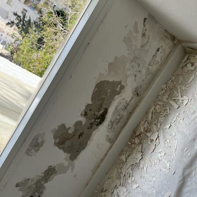 קיר מתקלף עם סימני רטיבות ליד חלון