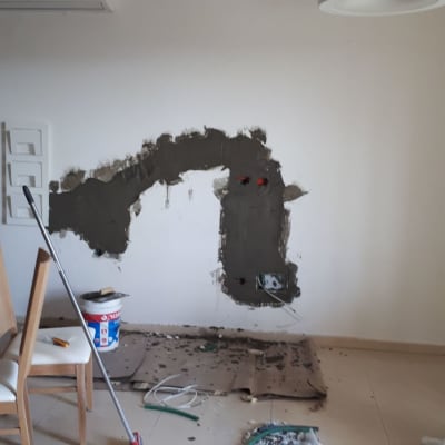 קיר בשיפוץ עם טיח, דלי וכלים על הרצפה