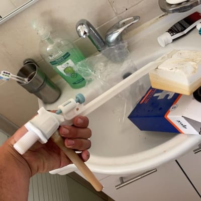 יד מחזיקה חלק פלסטיק לבן ליד כיור עם כלים