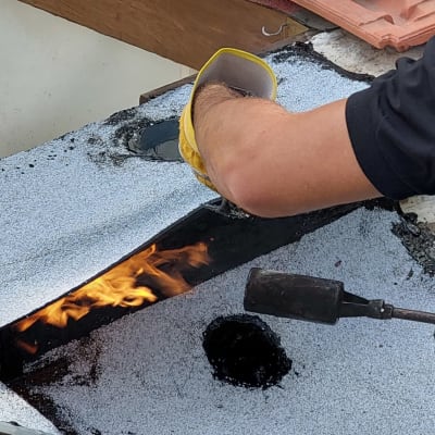 אדם משתמש במבער לאיטום גג עם יריעות ביטומניות