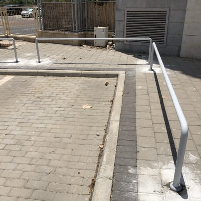 מעקה מתכת אפור על מדרכה מרוצפת