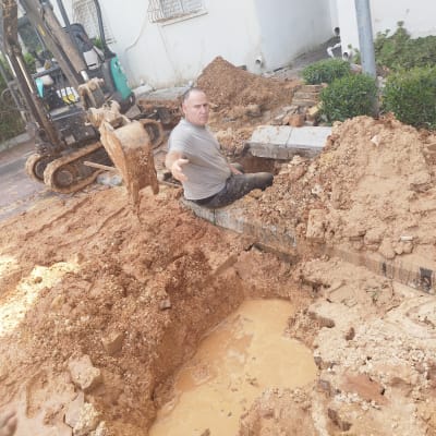 אדם עובד בתעלה עם מים ובוץ, חופר עם מחפרון