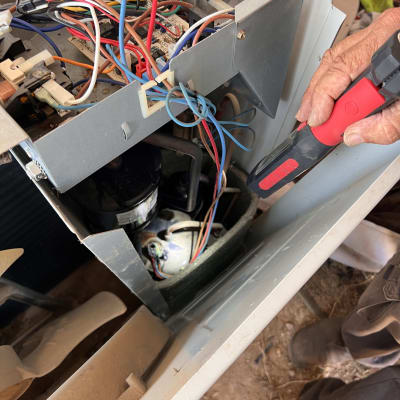 אדם מתקן מזגן עם כלי עבודה וחוטי חשמל