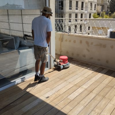 אדם משייף רצפת עץ במרפסת עם מכונה חשמלית