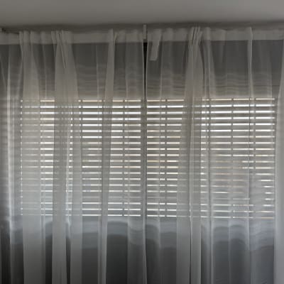 וילון לבן מול חלון עם תריסים