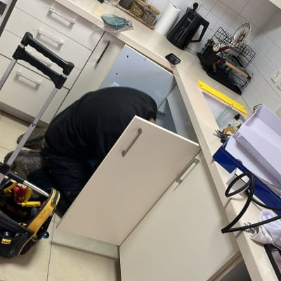 אינסטלטור עובד מתחת לכיור במטבח עם כלי עבודה