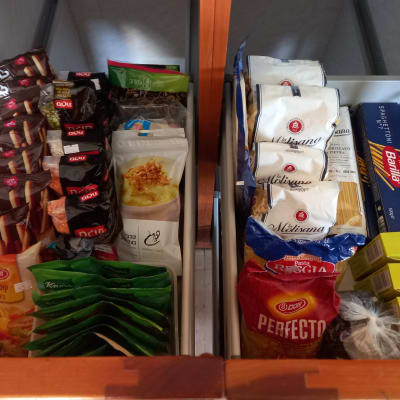 מגוון מוצרי מזון מאורגנים במגירה, כולל פסטה ותבלינים.