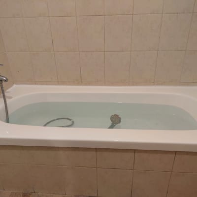 אמבטיה עם מים וברז מתכת על קיר מרוצף