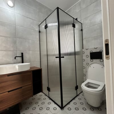 מקלחון זכוכית עם דלתות שחורות, כיור עץ ואסלה בחדר אמבטיה מודרני