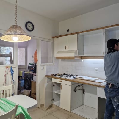 מטבח בשיפוץ עם ארונות פתוחים ואדם בעבודה