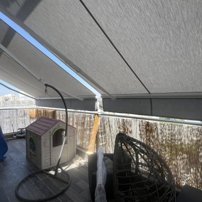 סוככים אפורים נמתחים מעל מרפסת עם נוף עירוני.