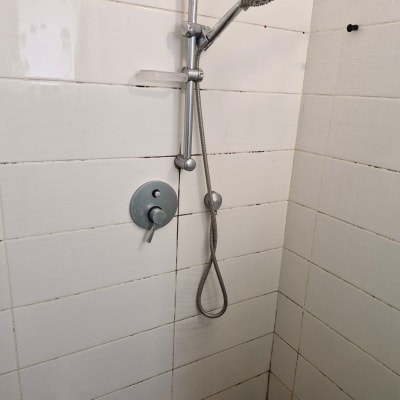 מקלחת עם אריחים לבנים וראש מקלחת מתכתי