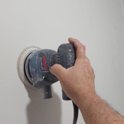 יד מחזיקה מלטשת חשמלית על קיר לבן