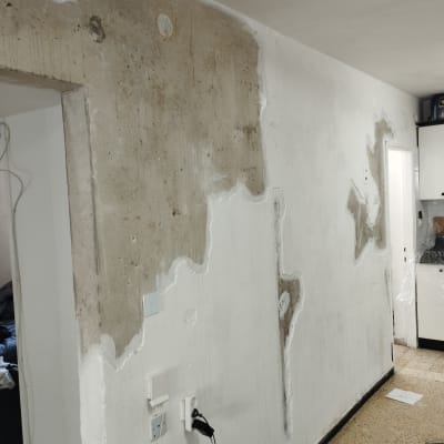 קיר עם טיח מתקלף וחומרי תיקון על הרצפה