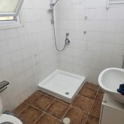 אגנית לבנה למקלחון ומערכת ברזים בחדר רחצה