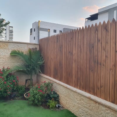 גדר עץ גבוהה עם צמחים ופרחים בגינה קטנה