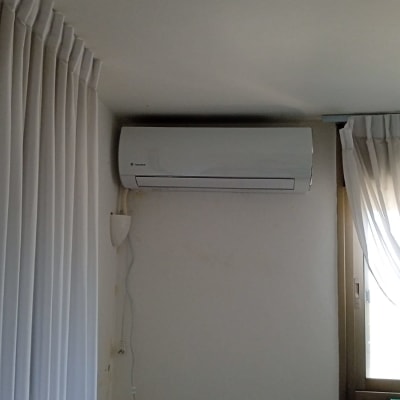 מזגן מותקן על קיר ליד חלון עם וילון לבן